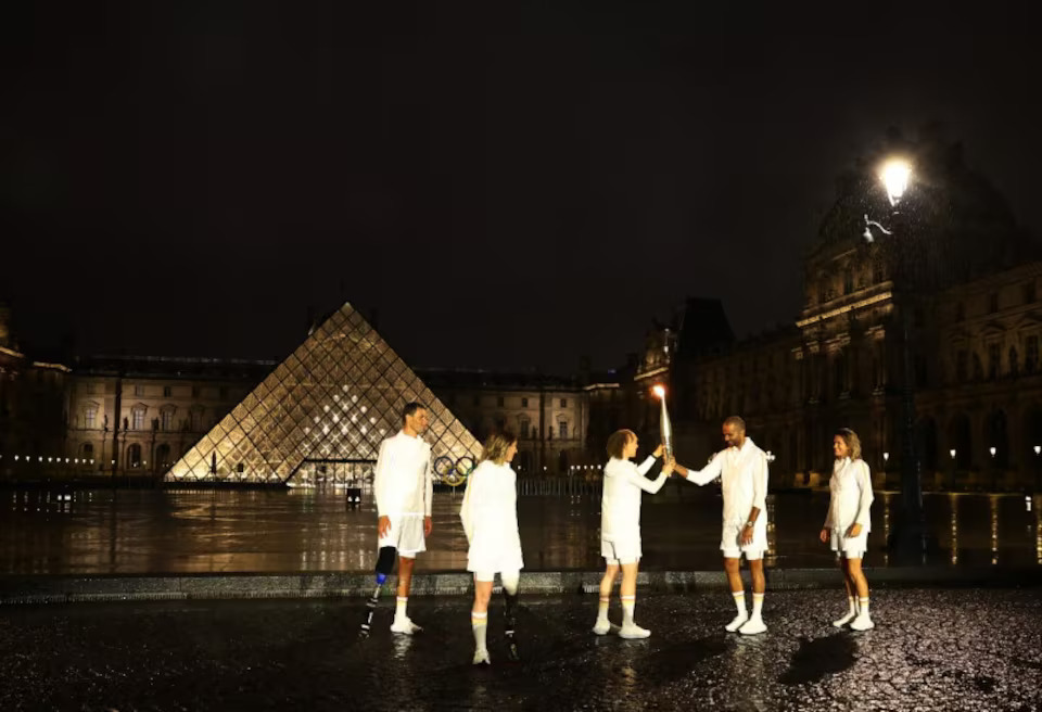 [12/12]Paris 2024 Olympics - Opening Ceremony - Paris, France - July 26, 2024. Paralympic sprinter Nantenin Keita and former basketball player Tony Parker hold the Olympic torch at the Louvre during the opening ceremony of the Paris 2024 Olympics. Photo: Reuters