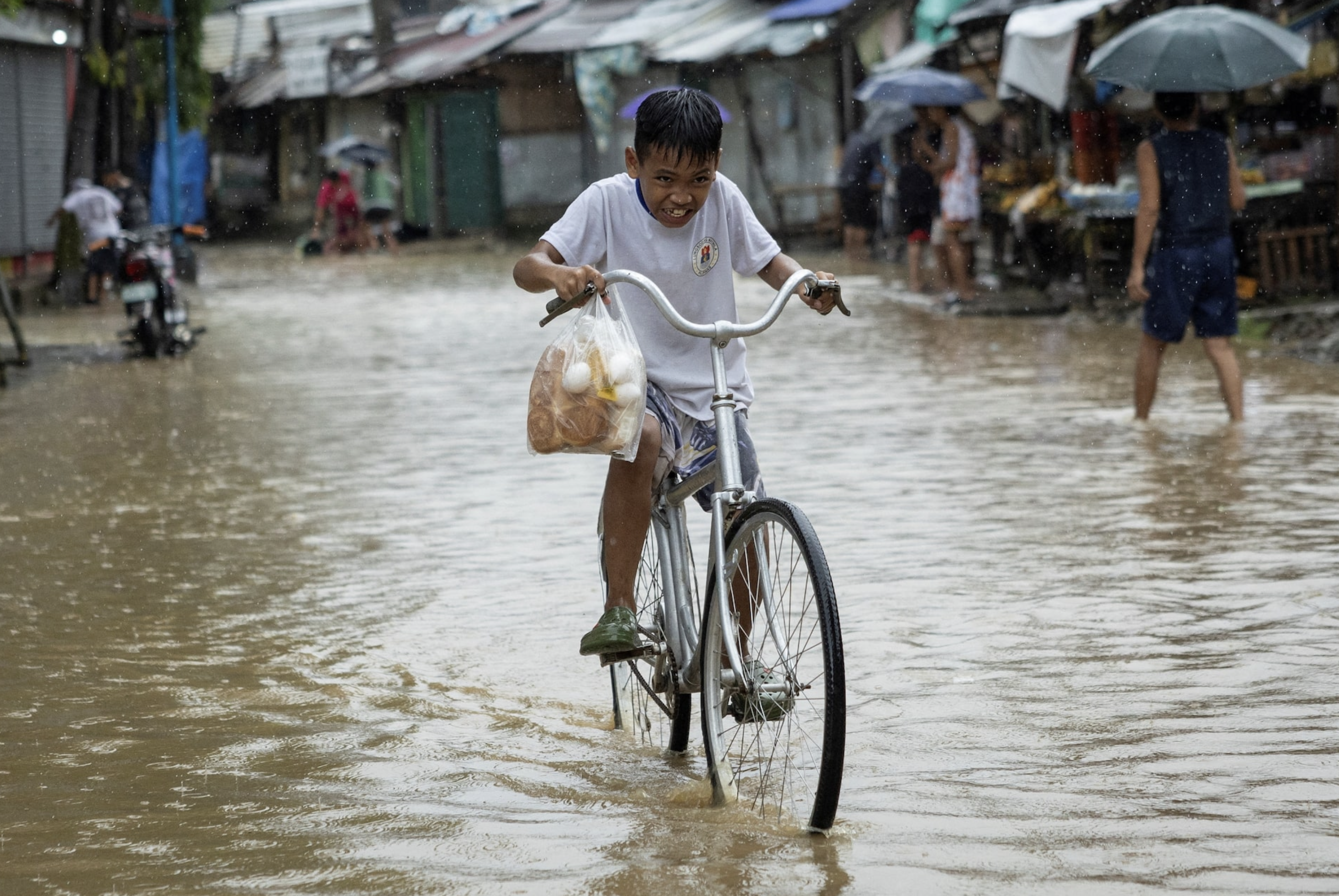 A boy carrying a plastic bag with bread and eggs, rides his bike through a flooded road after heavy rains brought by Tropical storm Yagi, locally known as Enteng, in Baras, Rizal province, Philippines, September 2, 2024. Photo: Reuters