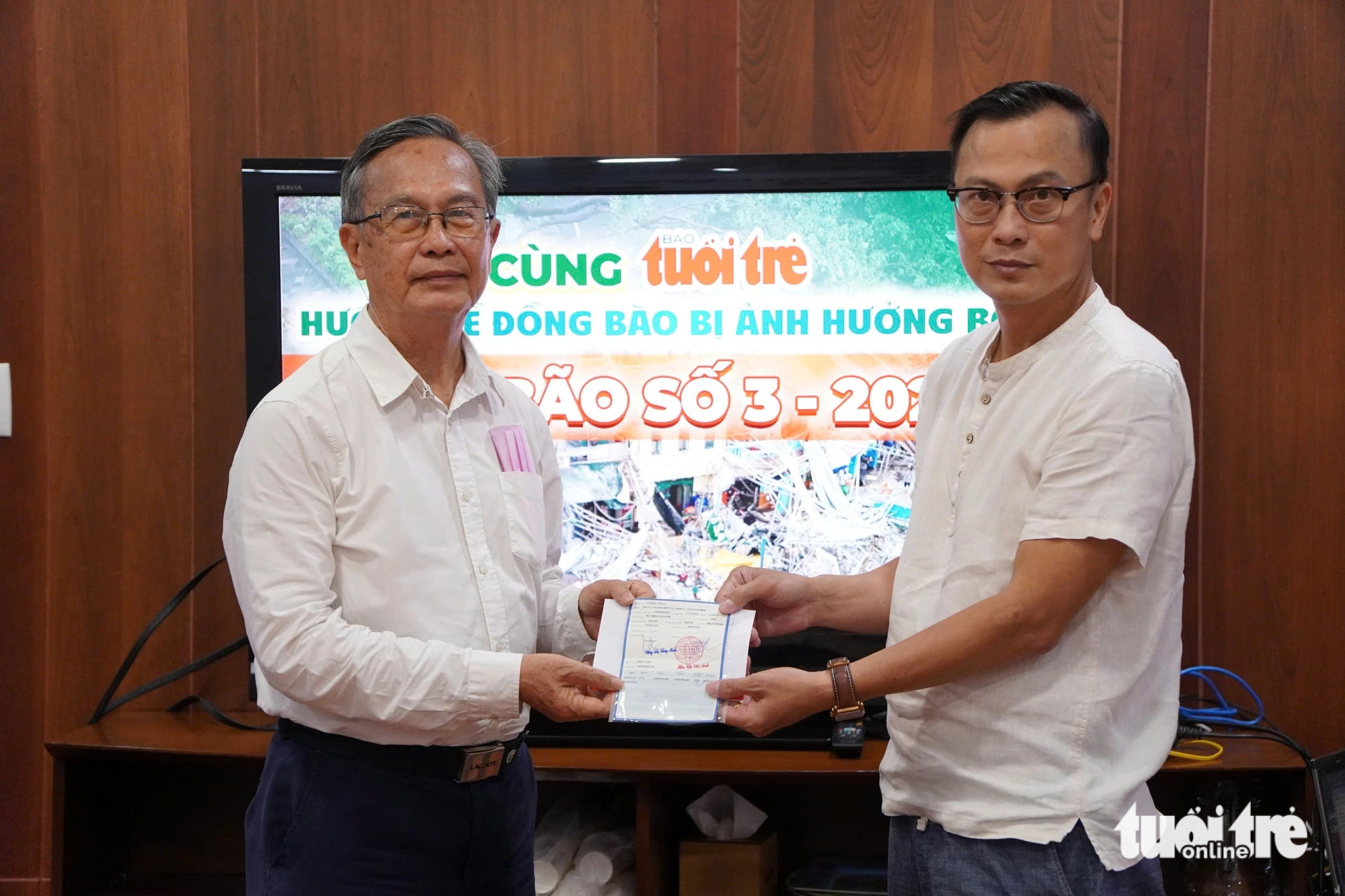 Prof. Dr. Le Ngoc Thach (L) delivers his savings book worth VND1 billion (US$40,716) to Tuoi Tre (Youth) newspaper's representative at its headquarters in Phu Nhuan District, Ho Chi Minh City, September 10, 2024. Photo: An Vi / Tuoi Tre