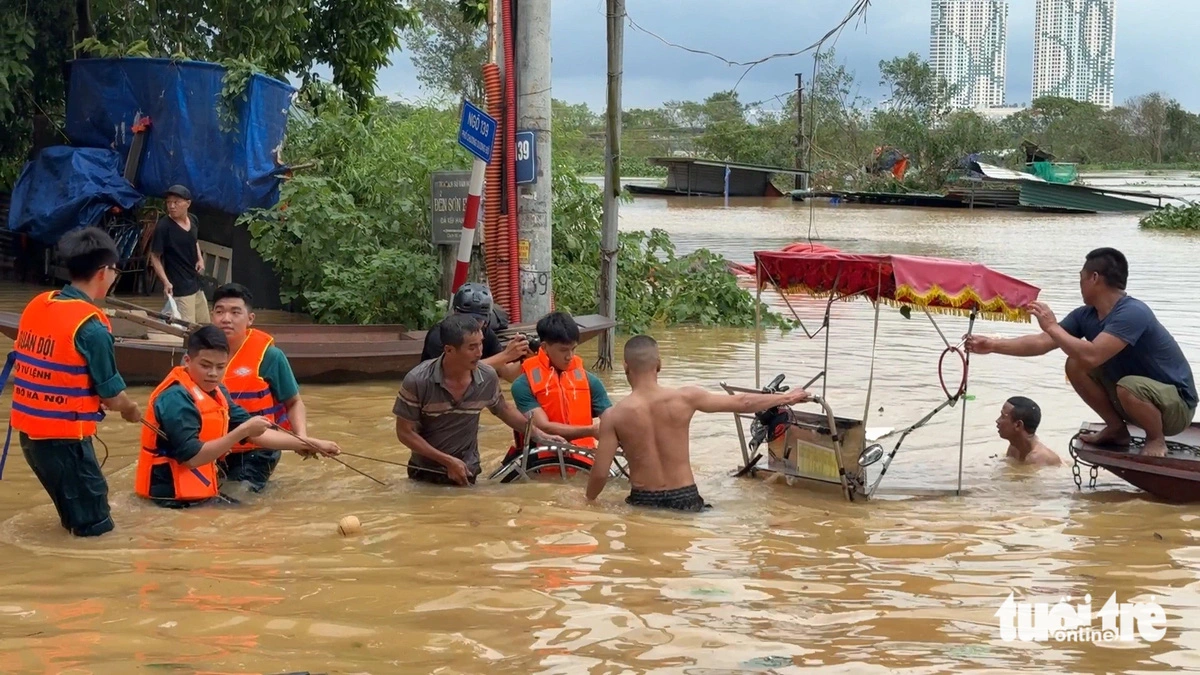 This image shows soldiers helping people in Hanoi, northern Vietnam to move a vehicle up from a heavily submerged area following the rise of the Red River. Photo: Pham Tuan / Tuoi Tre