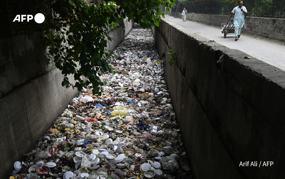 A labourer walks past a drain filled with plastic items in Lahore on September 6, 2024. Photo: AFP