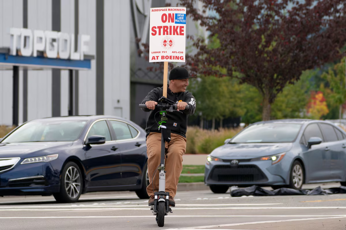 A person holds a strike sign while riding a scooter as Boeing factory workers and supporters gather on a picket line near the entrance to a Boeing production facility in Renton, Washington, U.S. October 11, 2024. Photo: Reuters