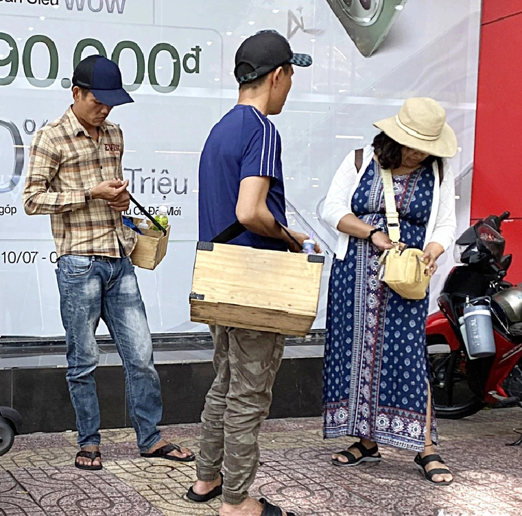 Two shoeblacks approach a tourist on Le Loi Street in Ho Chi Minh City.