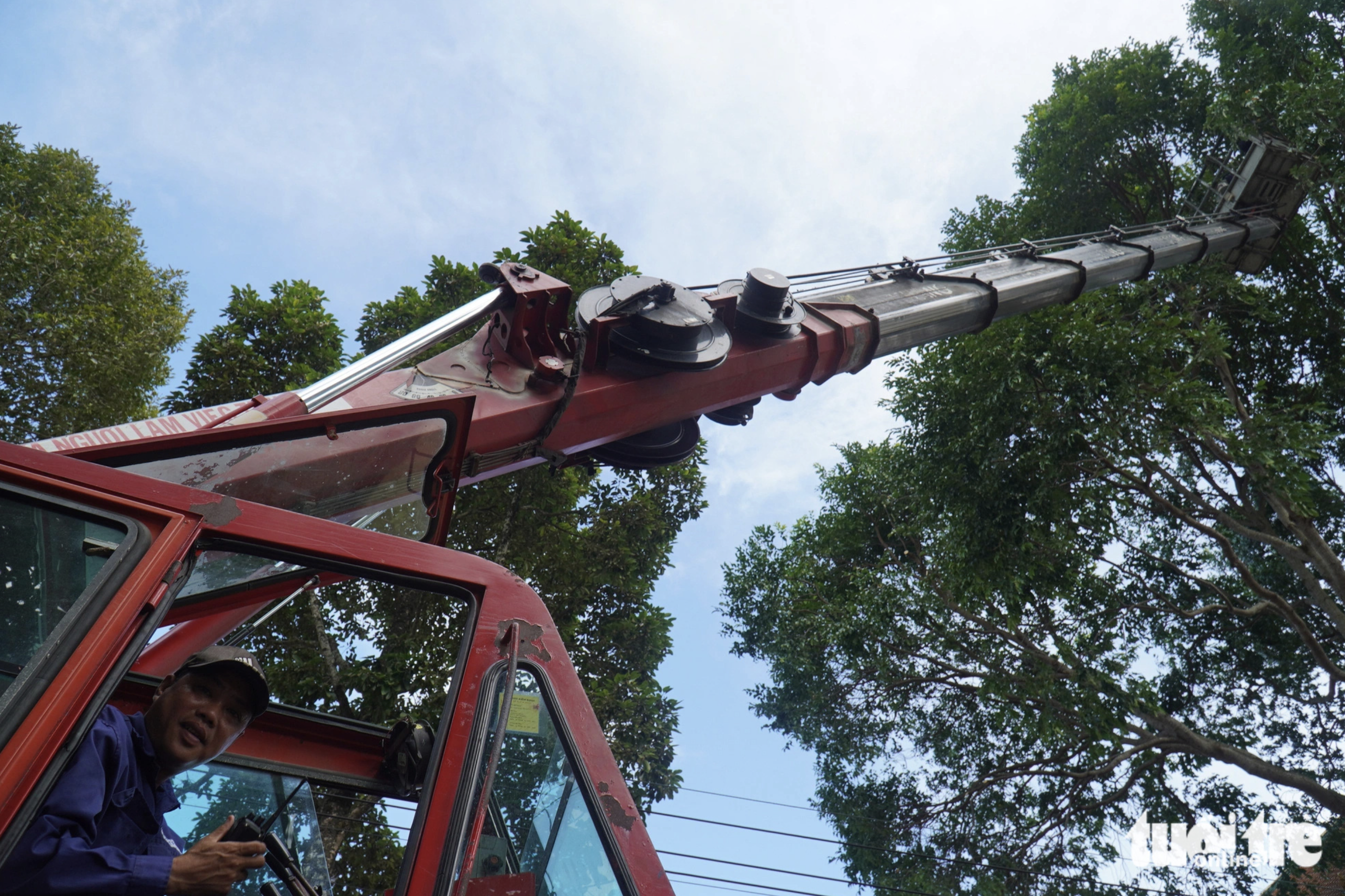 Pham Chi An, an employee at a street tree care company in Tra Vinh City, is pictured controlling an aerial lift to thin out trees to prevent their branches from falling down. Photo: Mau Truong / Tuoi Tre