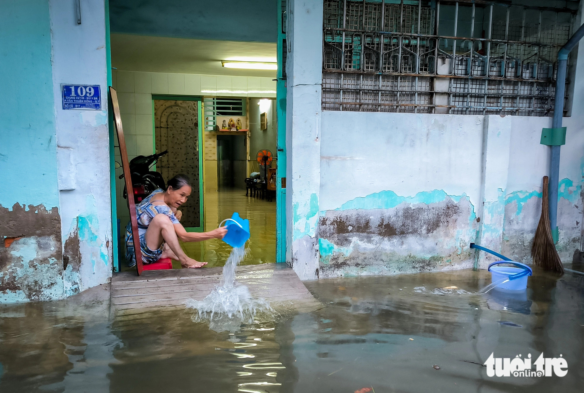 A woman splashes water out of her home down the flooded Alley 67 on Bui Van Ba Street in District 7, Ho Chi Minh City, October 18, 2024. Photo: Le Phan / Tuoi Tre