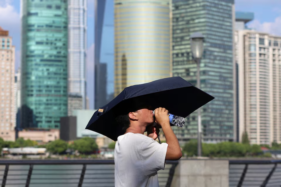 A man drinks from a water bottle under an umbrella as he walks on The Bund amid a red alert for heatwave, in Shanghai, China August 1, 2024. Photo: Reuters