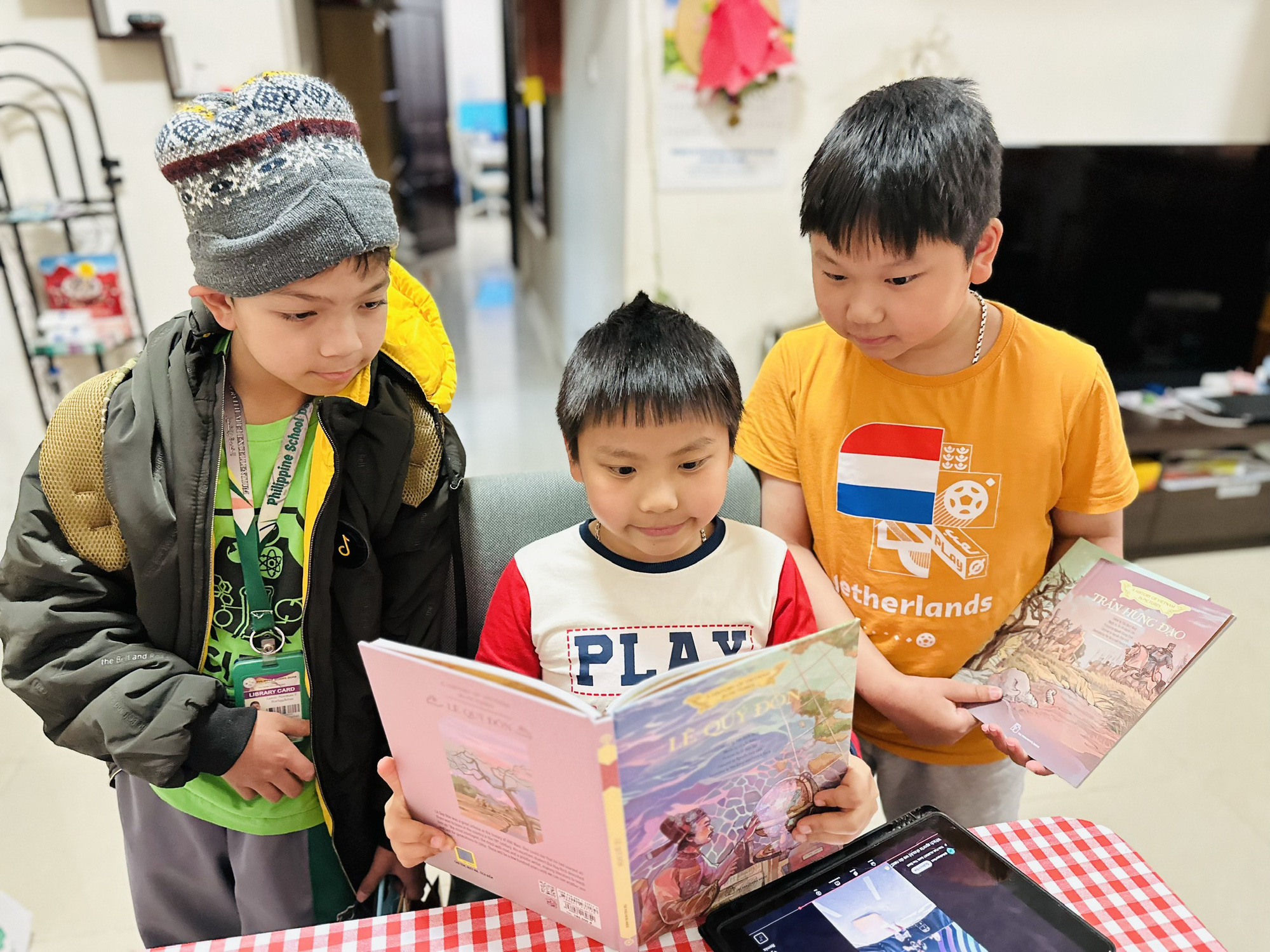 Vietnamese students Nguyen Ngoc Gia Bao (R) and Nguyen Gia Hoang (C), along with Filipino student Lanze Norman P. Borlagdatan, from the Philippine Doha School, read the English version of a picture book about Vietnamese history in Doha. Photo: Trung Nghia