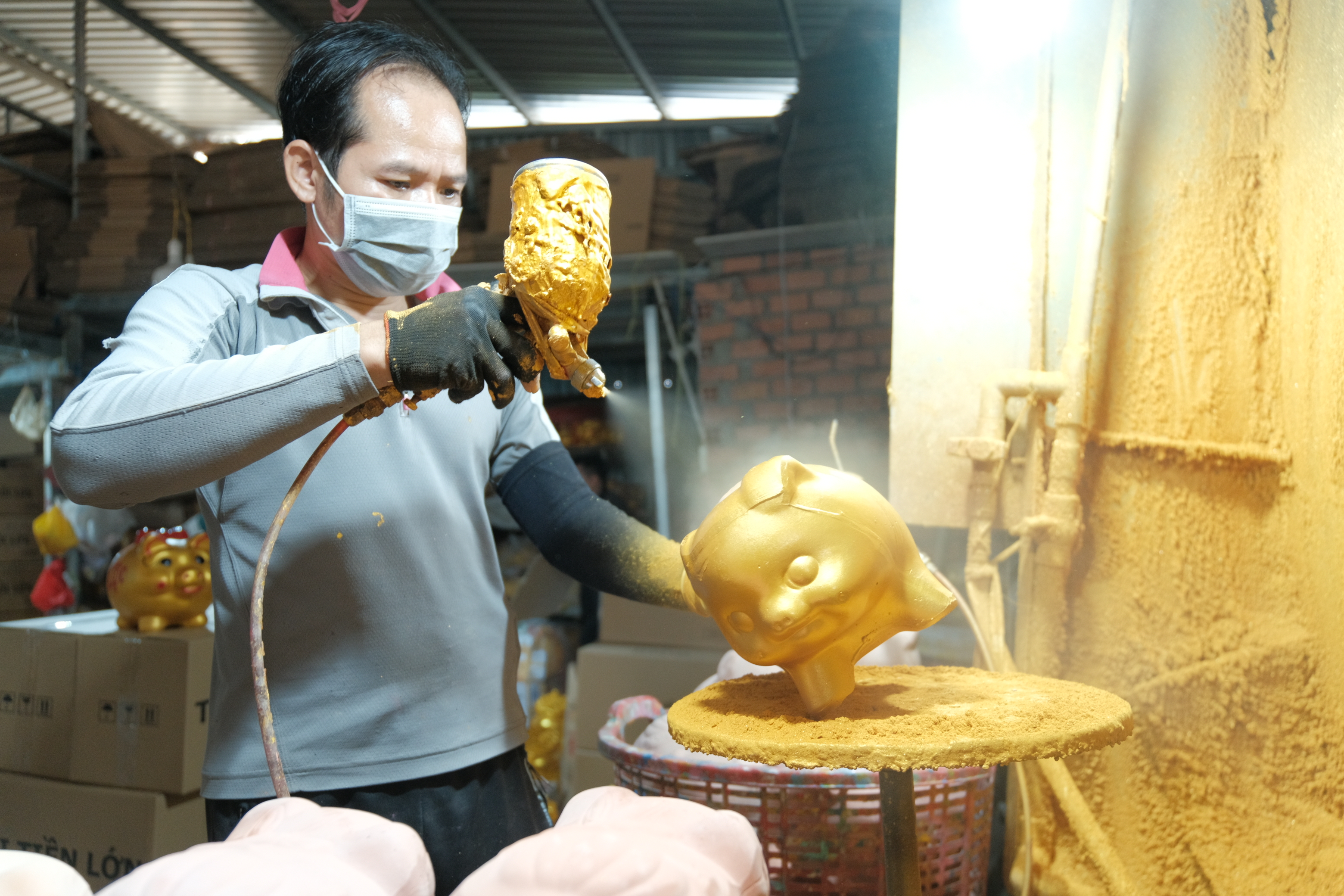 A worker sprays a golden shimmer onto traditional piggy banks, symbolizing prosperity and good fortune. Photo: Ngoc Phuong / Tuoi Tre News