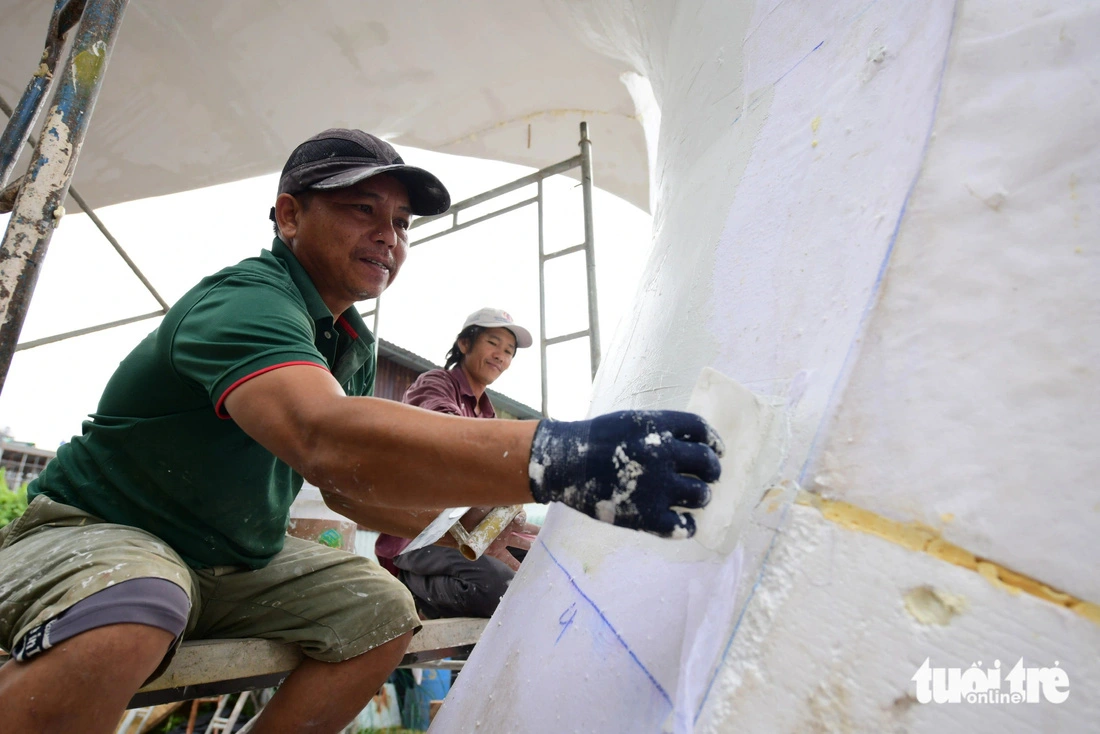 A worker applies a mixture of plaster and glue to harden the snake mascot's body, ensuring it won't crack in the sun. The scales of this year's snake mascots require meticulous attention from workers.