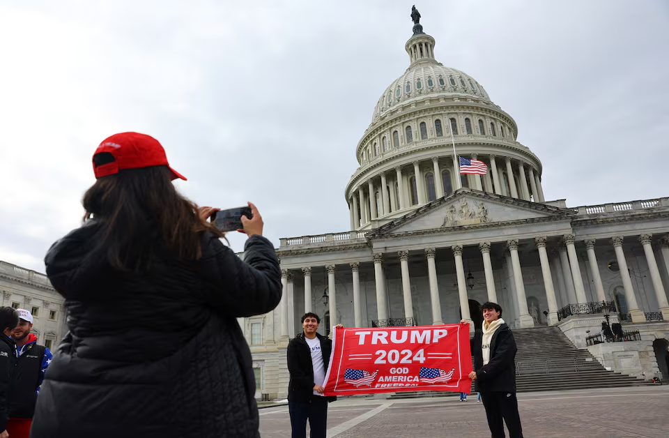 A woman uses a mobile phone as people hold a placard in favour of U.S. President-elect Donald Trump in front of the U.S. Capitol building ahead of the presidential inauguration in Washington, U.S., January 18, 2025. Photo: Reuters