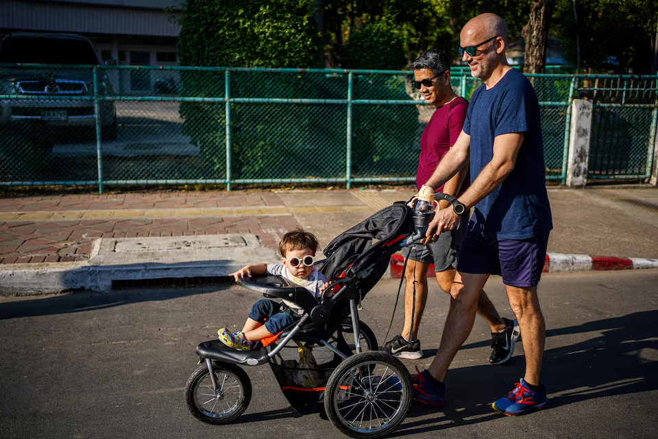 A gay couple, Surapong 'Keng' Koonpaew, 48, and Jacob Holder, 45, walk as their son Elijah Bprin Holder Koonpaew sits on a baby cart at a park in Bangkok, Thailand, January 11, 2025. Photo: Reuters