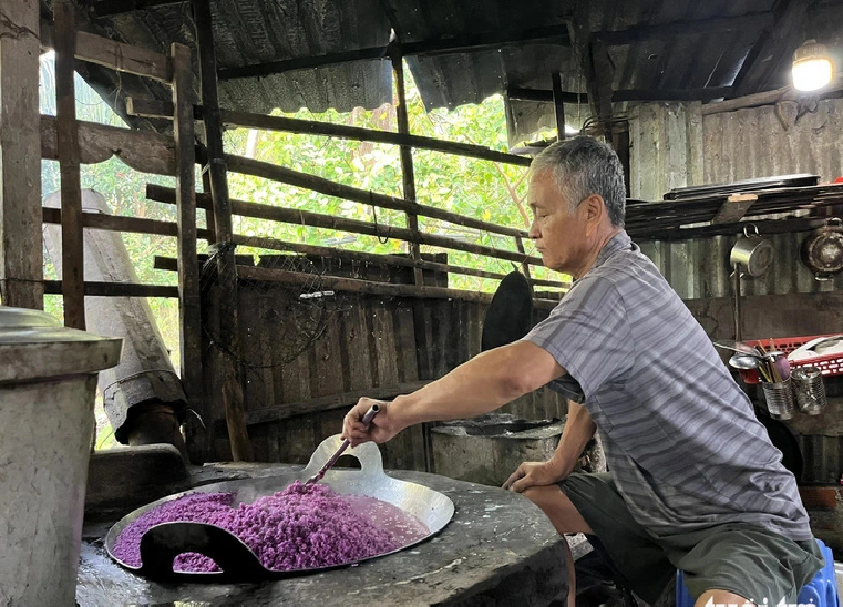 A man prepares glutinous rice mixed with the purple water from magenta leaves.