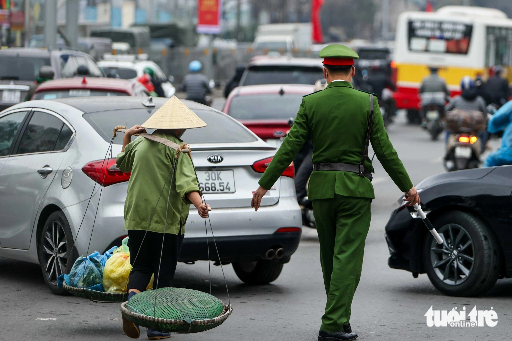 A police officer helps a street hawker cross the street in Hanoi, January 25, 2025. Photo: Nguyen Khanh / Tuoi Tre