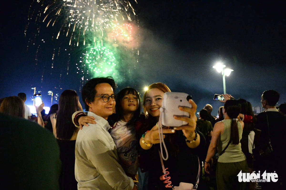 A young woman takes a selfie with her husband and young daughter beneath the fireworks in Ho Chi Minh City. Photo: Hai Quynh