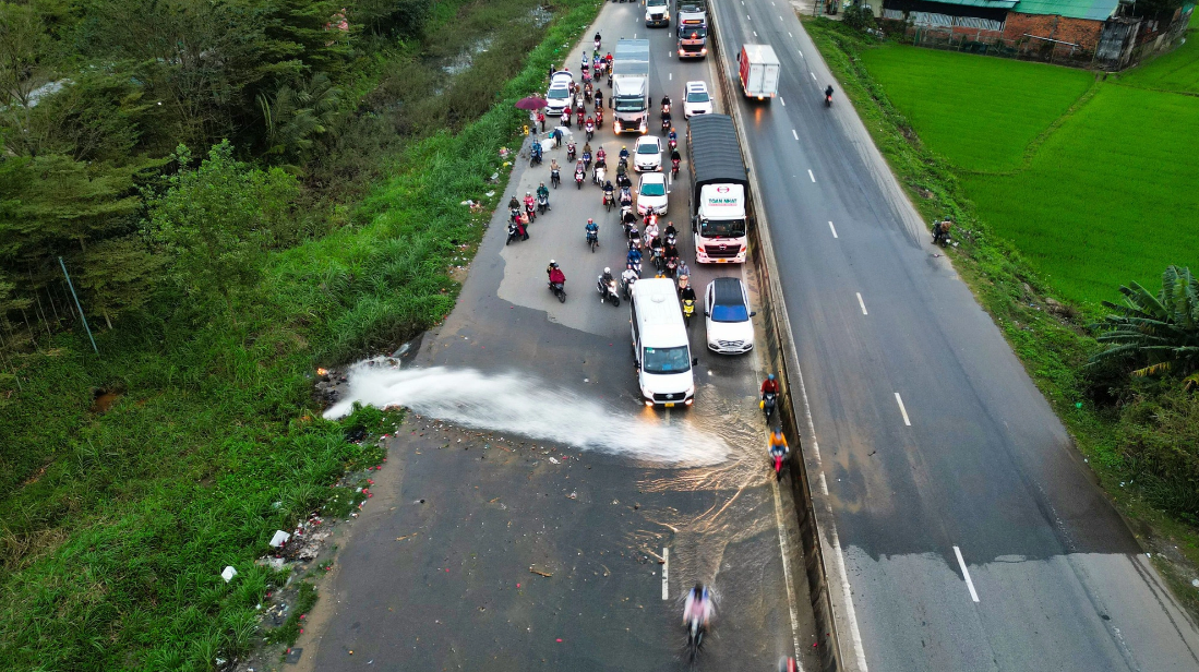 A pipe bursts and a jet of water sprays directly onto a section of National Highway 1 in Quang Ngai Province, central Vietnam, making it tough for motorcyclists to pass through. Photo: Anh Don