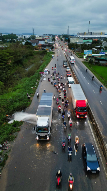 A container truck driver is praised for his act of kindness as he uses his vehicle as a barrier for motorcyclists to pass through a flooded section of National Highway 1 in Quang Ngai Province, central Vietnam after a pipe breaks. Photo: Anh Don