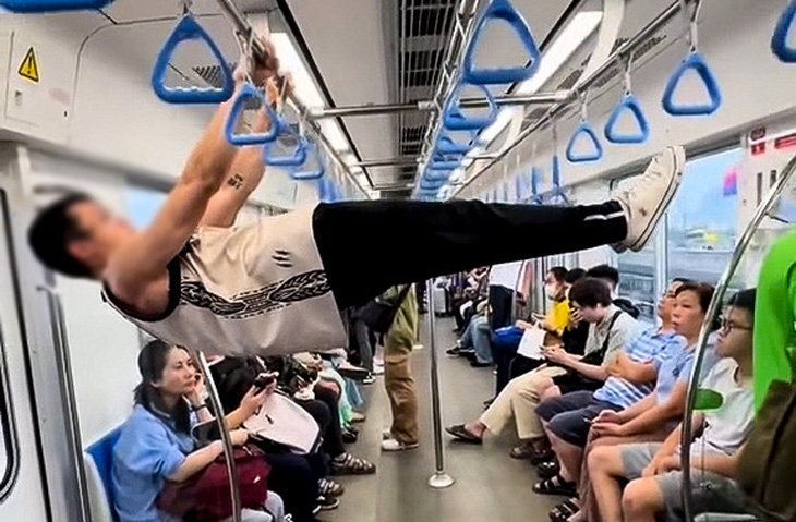 A screenshot from a video shows a man using the handrails and ceiling bars to perform gymnastic moves and pull-ups on metro line No. 1 in Ho Chi Minh City.