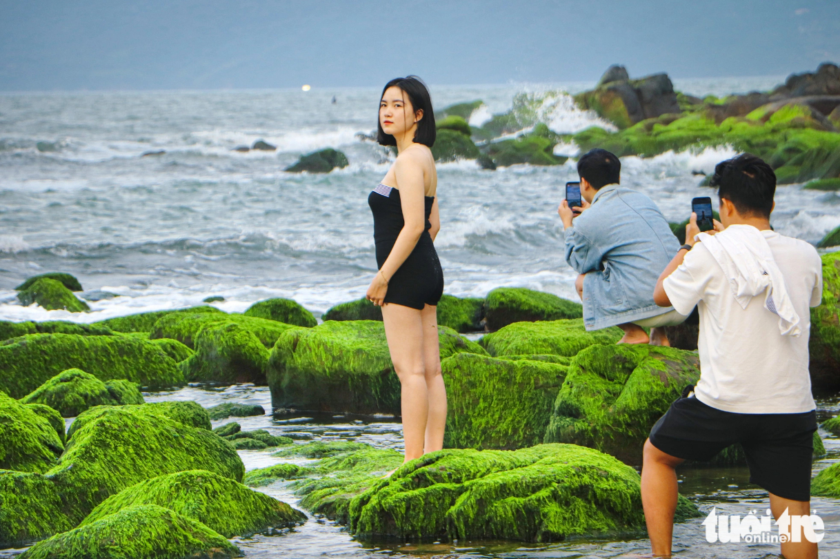 A girl poses for a photo on moss-covered rocks at Nam O Beach in Da Nang City, central Vietnam. Photo: Thanh Nguyen / Tuoi Tre