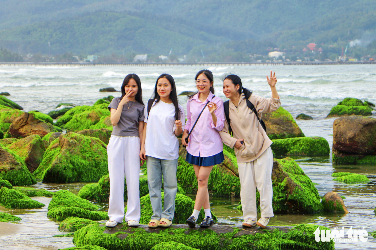 A group of young people poses for a photo with green moss-covered rocks along Nam O Beach, Da Nang City, central Vietnam. Photo: Thanh Nguyen / Tuoi Tre