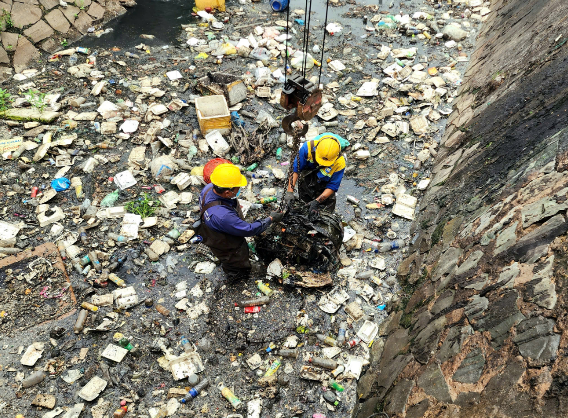 Two sanitation workers collect waste and then place it into a basket for a crane to lift at a stretch of Canal 19/5 in Tan Phu District, Ho Chi Minh City. Photo: Ngoc Khai / Tuoi Tre