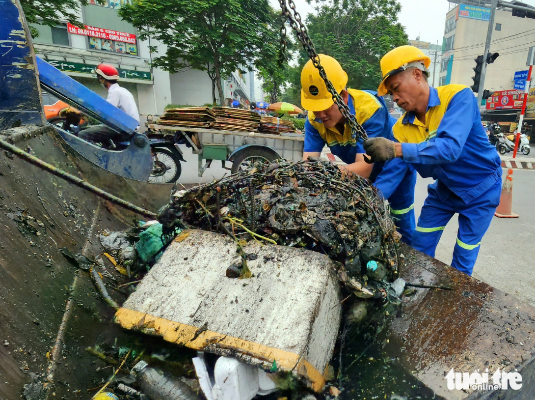 Two sanitation workers pour trash onto a trash truck after removing it from Canal 19/5. Photo: Ngoc Khai / Tuoi Tre