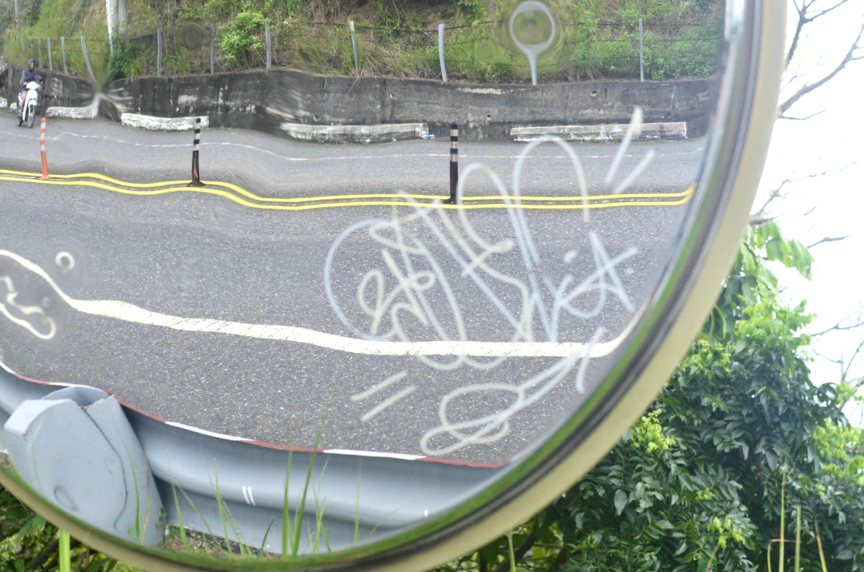 A convex mirror is vandalized with graffiti.