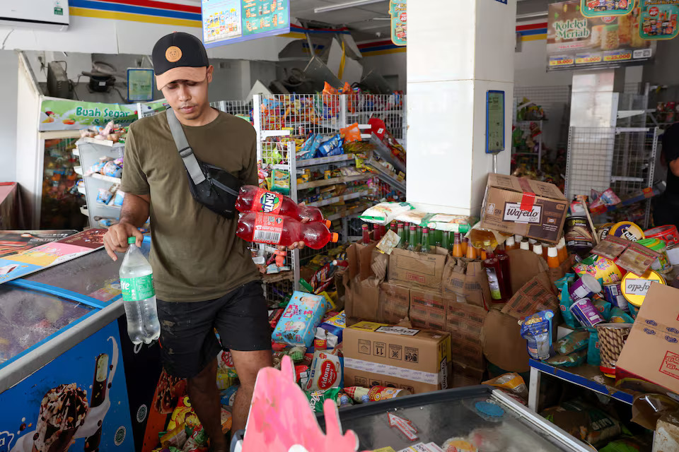 [7/10]A resident carries sparkling drinks from the damaged market as floods hit the residential area following heavy rains in Bekasi, on the outskirts of Jakarta, Indonesia, March 4, 2025. Photo: Reuters