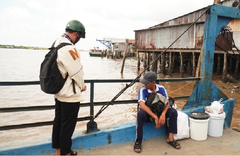 Do sits and rests at the ferry crossing the Cua Lon River in Ca Mau Province with two containers of leftover food and a bag of scrap metal. Photo: Thanh Huyen / Tuoi Tre