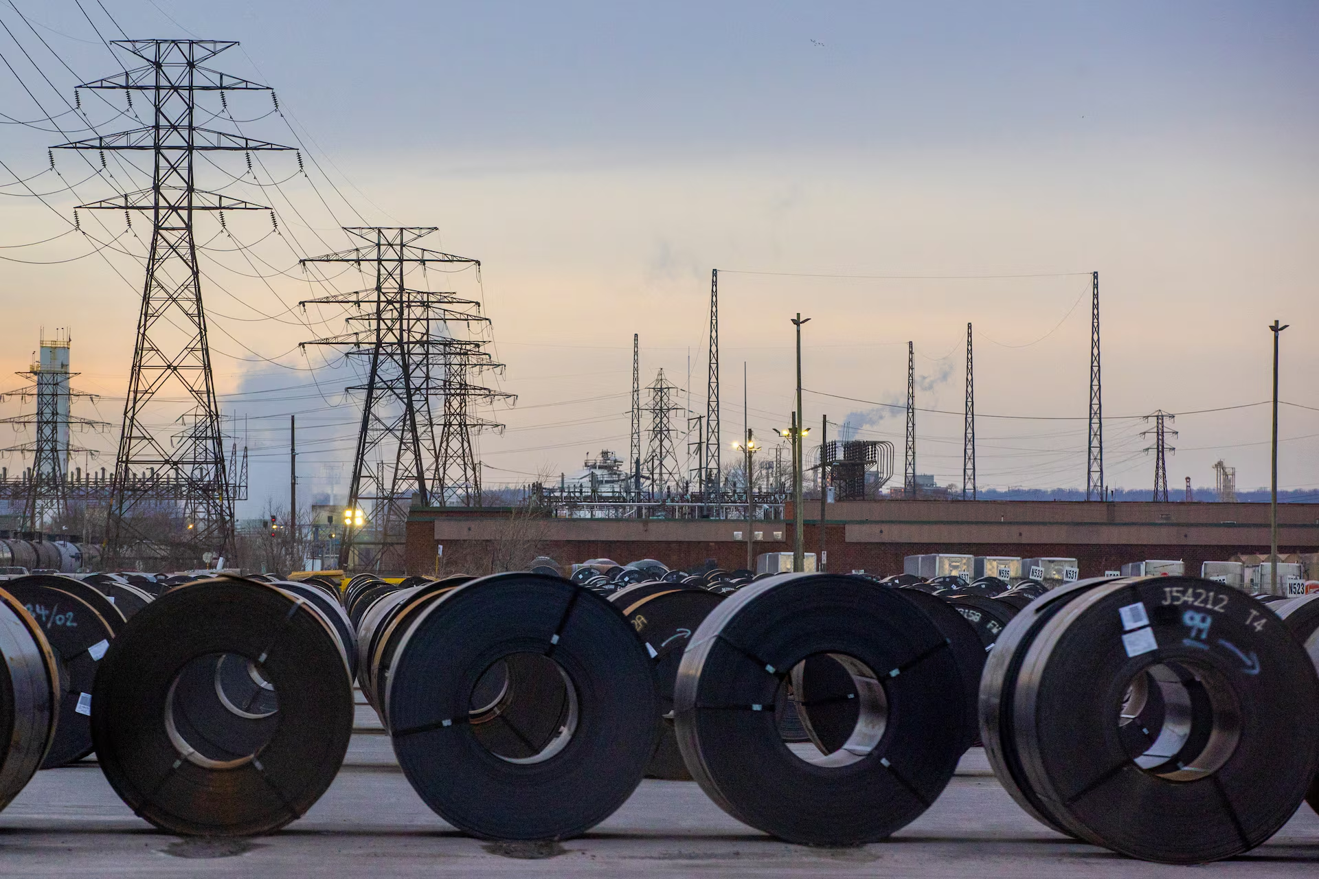 Coils of rolled steel sit in an industrial yard with transmission towers and smokestacks in the background at dusk in Hamilton, Ontario, Canada, January 27, 2025. Photo: Reuters